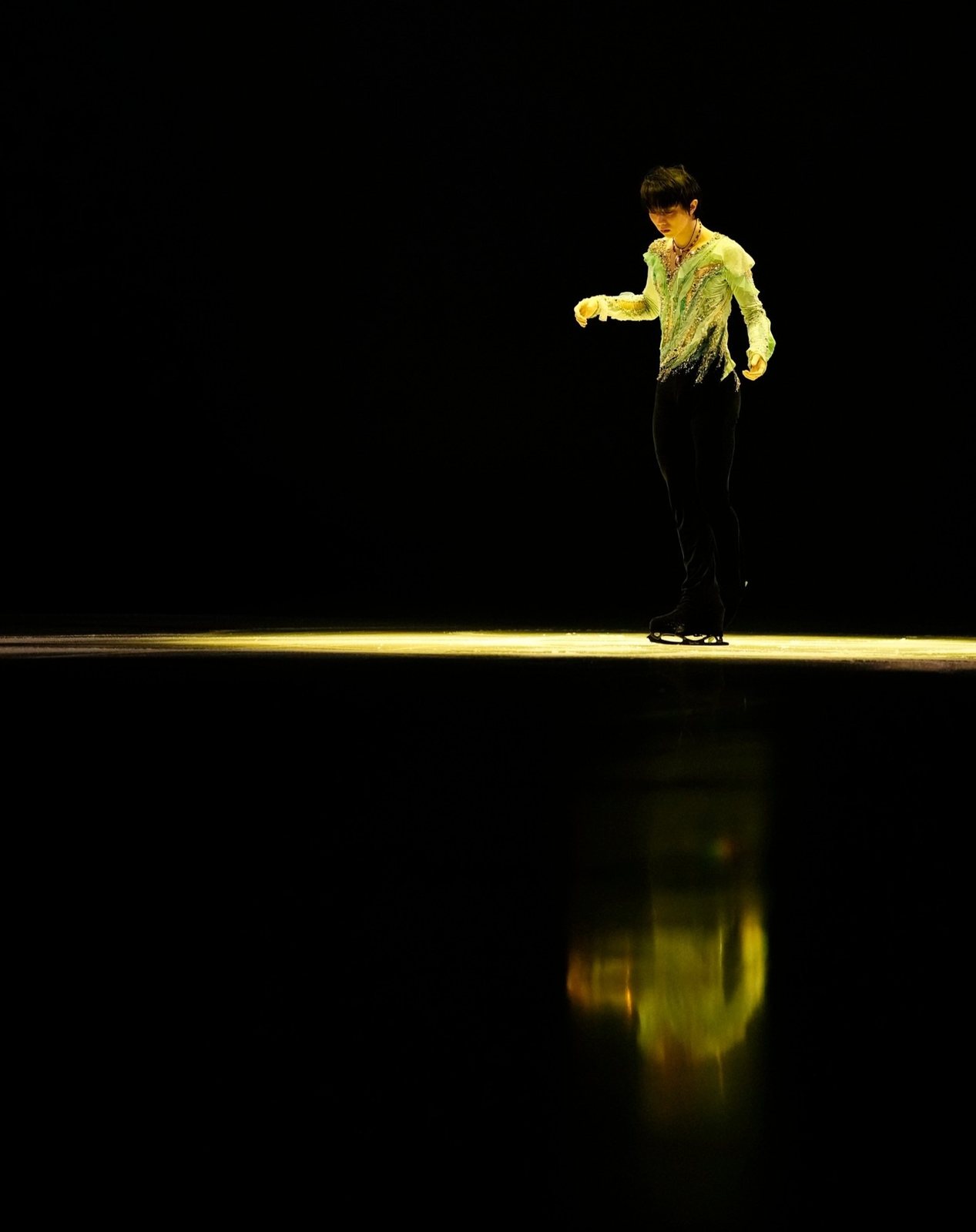 暗いリンクにひと筋の光。その中に立つ羽生結弦と、氷に映る姿