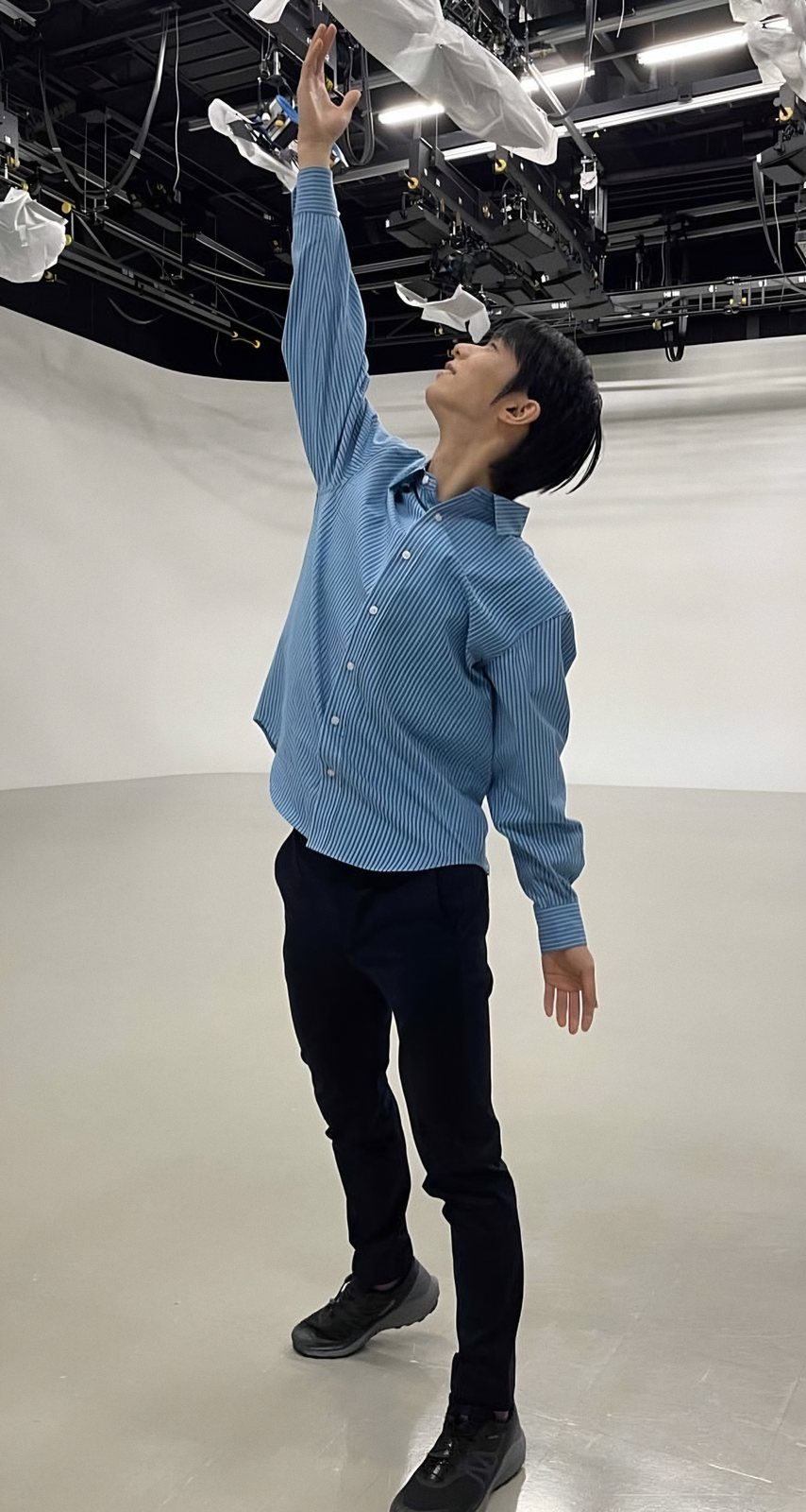 白いスタジオで、片腕を高く伸ばす羽生結弦